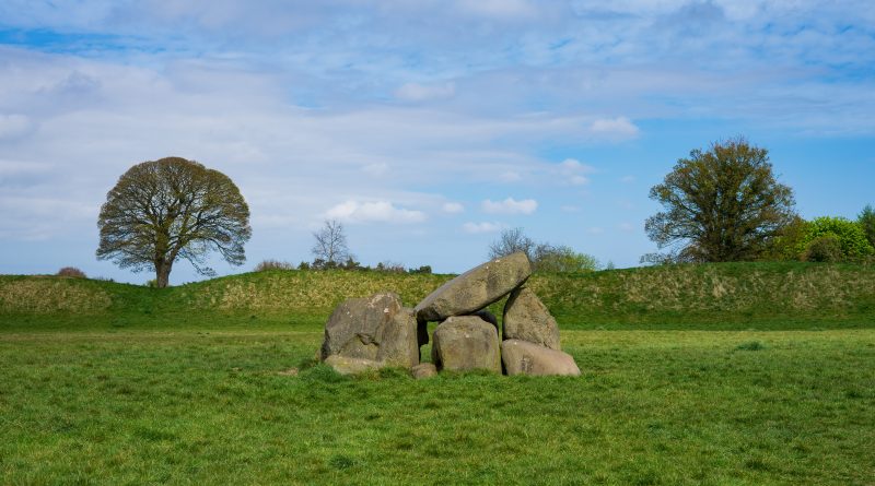 gray rock formation on green grass field under blue and white sunny cloudy sky during daytime